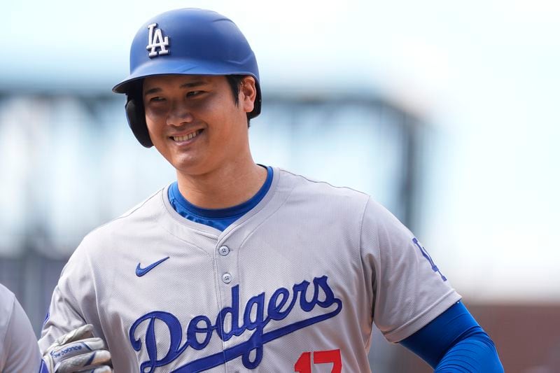 Los Angeles Dodgers' Shohei Ohtani smiles after reaching first base on a single off Colorado Rockies relief pitcher Seth Halvorsen in the eighth inning of a baseball game Sunday, Sept. 29, 2024, in Denver. (AP Photo/David Zalubowski)