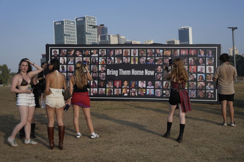People pause at a picture display of hostages held in the Gaza Strip at the Nova Healing Concert in Tel Aviv, Israel, on Thursday, June 27, 2024. This was the first Tribe of Nova mass gathering since the Oct. 7, 2023 cross-border attack by Hamas that left hundreds at the Nova music festival dead or kidnapped to Gaza. (AP Photo/Ohad Zwigenberg)