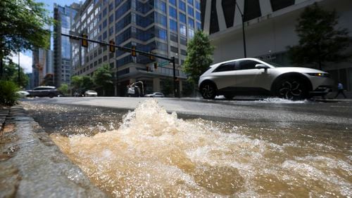 Automobiles travel on West Peachtree Street as water from a fire hydrant (behind SUV on the right) spills water in between 13th and 14th streets in Atlanta on Monday, June 3, 2024. (Jason Getz / AJC)