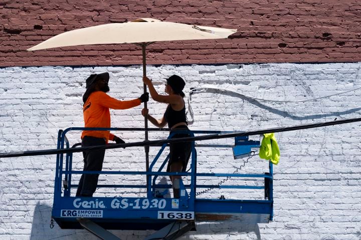 Andrea Alvarez, left, and Emily Cadena, with Overall Murals set up a shade umbrella to help keep cool while working on a mural along the Eastside Beltline in Atlanta on Monday, June 24, 2024.   (Ben Gray / Ben@BenGray.com)