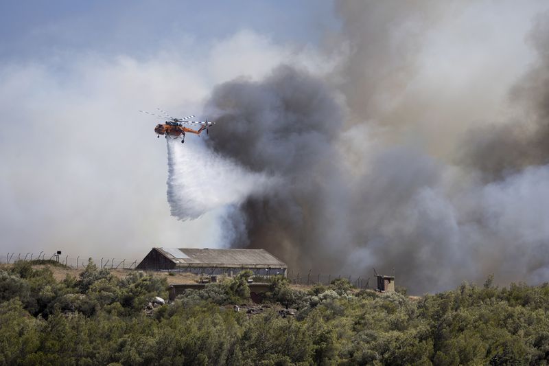 A firefighting helicopter drops water over a wildfire at Keratea area, southeast of Athens, Greece, Sunday, June 30, 2024. (AP Photo/Yorgos Karahalis)