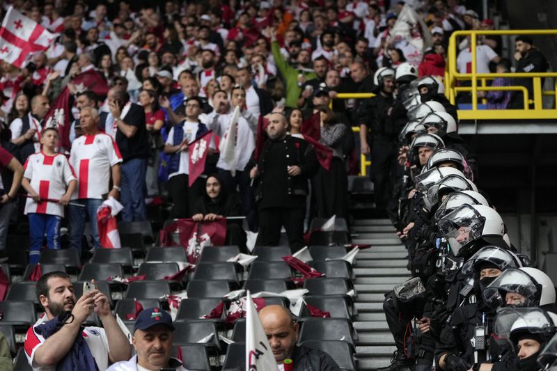 Police officers stand next Georgia's supporters prior to the start of a Group F match between Turkey and Georgia at the Euro 2024 soccer tournament in Dortmund, Germany, Tuesday, June 18, 2024. (AP Photo/Alessandra Tarantino)