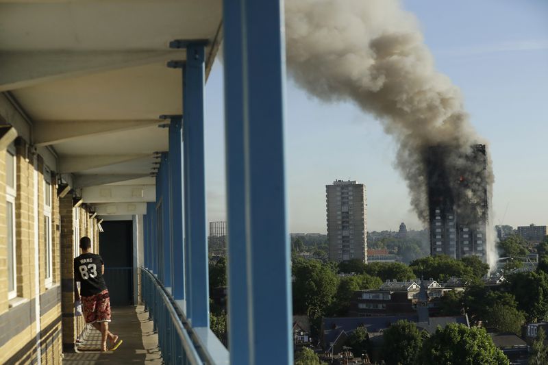 FILE - A resident in a nearby building watches smoke rise from the Grenfell Tower building on fire in London, Wednesday, June 14, 2017. (AP Photo/Matt Dunham, File)