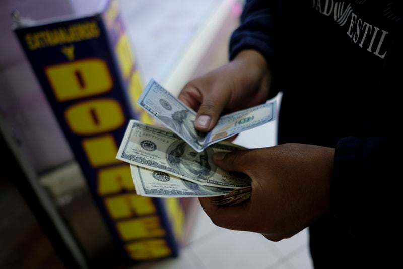 A man holds dollars at a currency exchange shop in La Paz, Bolivia, Friday, June 28, 2024, days after Army troops stormed the government palace in what President Luis Arce called a coup attempt. (AP Photo/Carlos Sanchez)