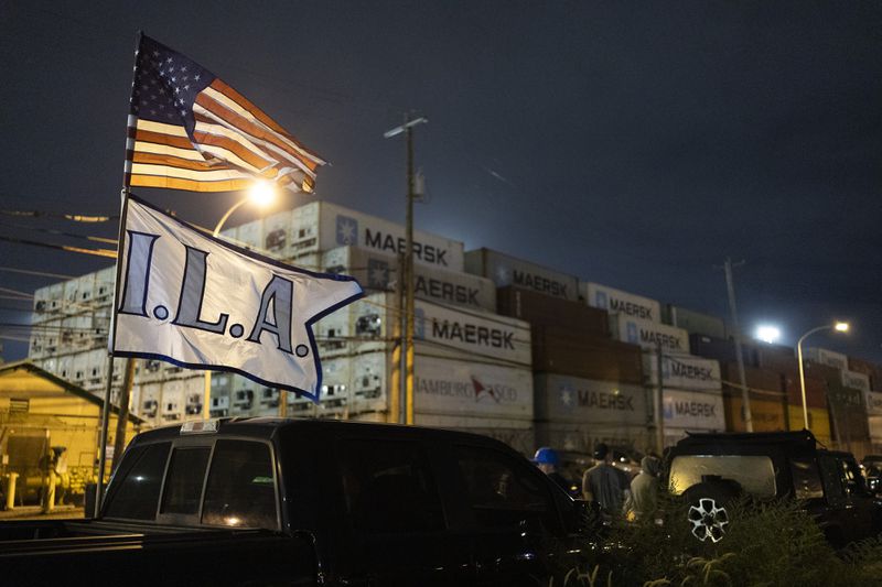 The International Longshoremen’s Association flag and an American flag fly together outside the Packer Avenue Marine Terminal Port as workers prepare to strike as their contract runs out at midnight, Monday, Sept. 30, 2024. (AP Photo/Ryan Collerd)