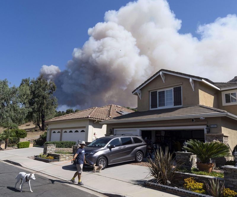 Ken Motonishi walks his dogs as the Airport Fire burns near Porter Ranch in Trabuco Canyon, Calif., on Tuesday, Sept. 10, 2024. (Paul Bersebach/The Orange County Register via AP)