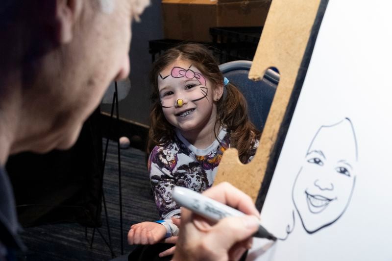 Esther Oratz, 4, grins as Mark Mandel draws a caricature of her during the Atlanta Jewish Life Festival at the Georgia Aquarium on Sunday.