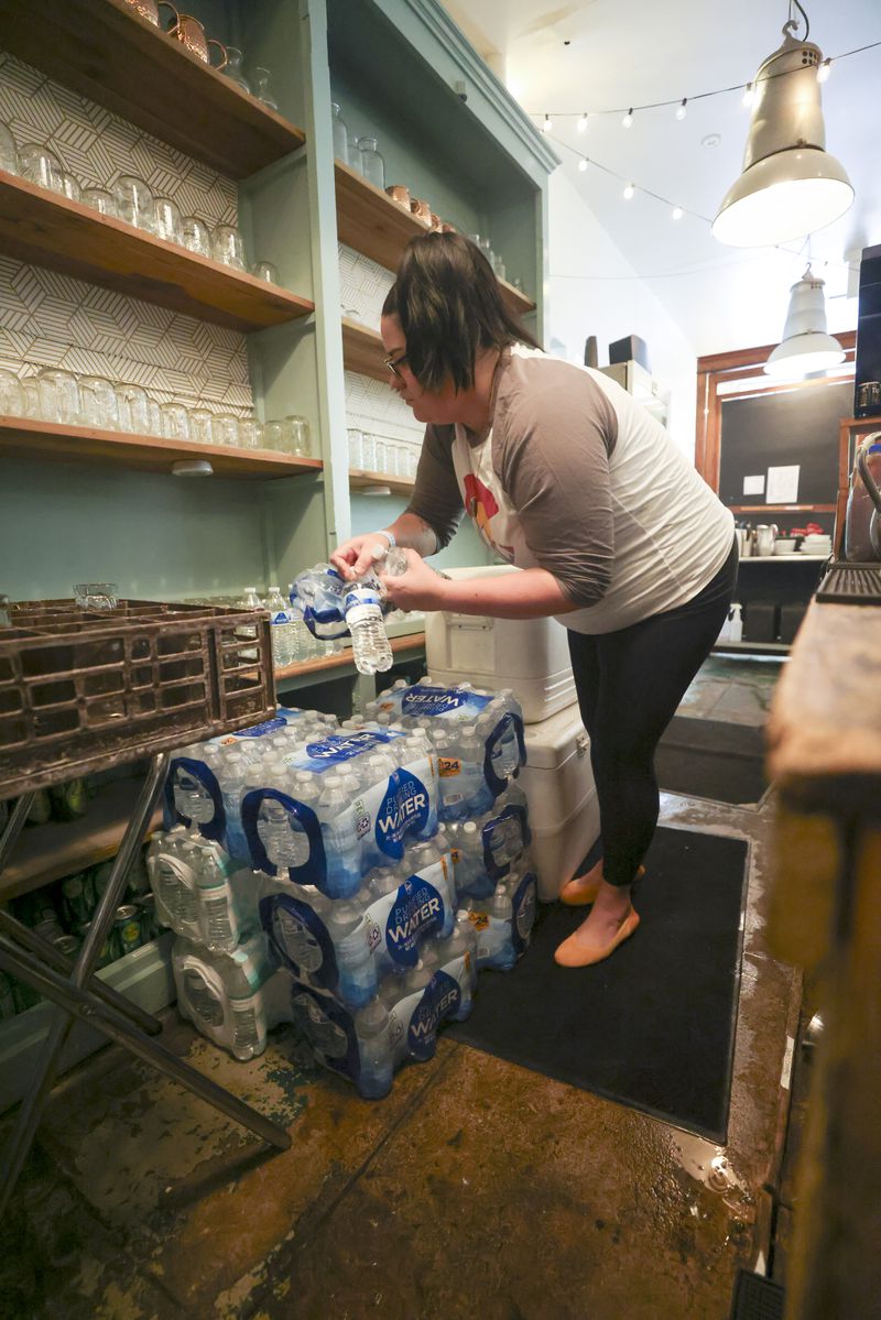 Sun in My Belly General Manager Megan Cook takes bottled water out of plastic bags for customers to use at the restaurant in the Kirkwood neighborhood, Monday, June 3, 2024, in Atlanta.  The restaurant always boils large pots of water in the kitchen and uses bottled water for service.  (Jason Getz/AJC)