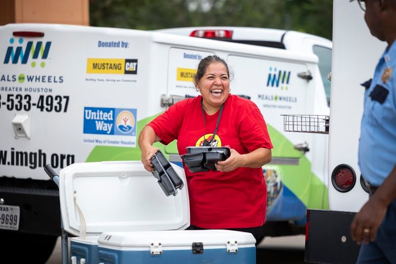 Meals on Wheels employee Yvette Gallaty smiles as she transfers hot meals from a cooler into her delivery truck before taking them to clients, Friday, July 12, 2024, in Houston. Gallaty always had office jobs but finds great joy in the physical, meaningful work she does for clients through Meals on Wheels. (AP Photo/Annie Mulligan)