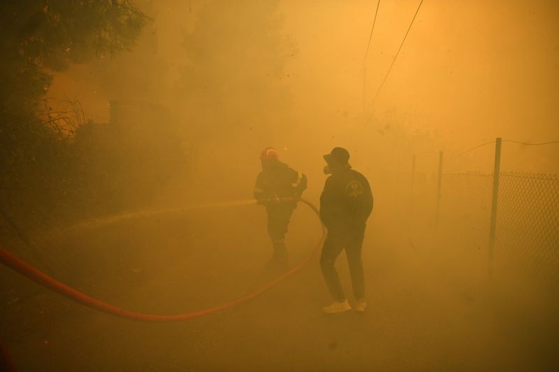 A firefighter and volunteer try to extinguish a fire in northern Athens, Monday, Aug. 12, 2024, as hundreds of firefighters tackle a major wildfire raging out of control on fringes of Greek capital. (AP Photo/Michael Varaklas)