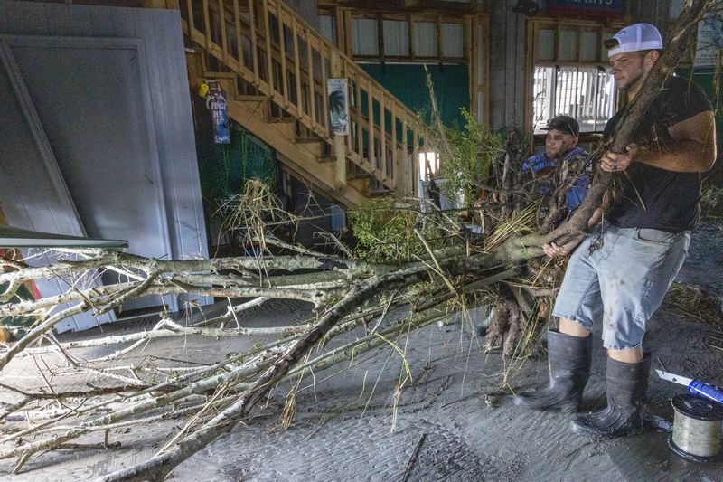 Jansen Pellegrin, back right, and Drew Foret, right, remove a small tree that floated into a living room area at their fishing camp from Hurricane Francine in Terrebonne Parish, La., Thursday, Sept. 12, 2024. (Chris Granger/The Times-Picayune/The New Orleans Advocate via AP)