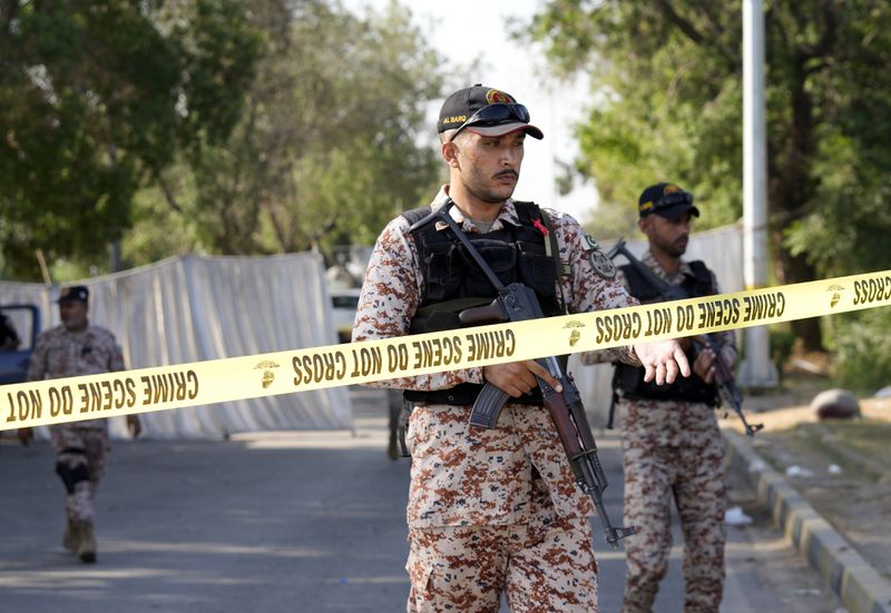 Security officials stand guard at the site of an explosion that caused injures and destroyed vehicles outside the Karachi airport, Pakistan, Monday, Oct. 7, 2024. Pakistani Baloch separatists claim deadly bomb attack that killed 2 Chinese near Karachi airport. (AP Photo/Fareed Khan)