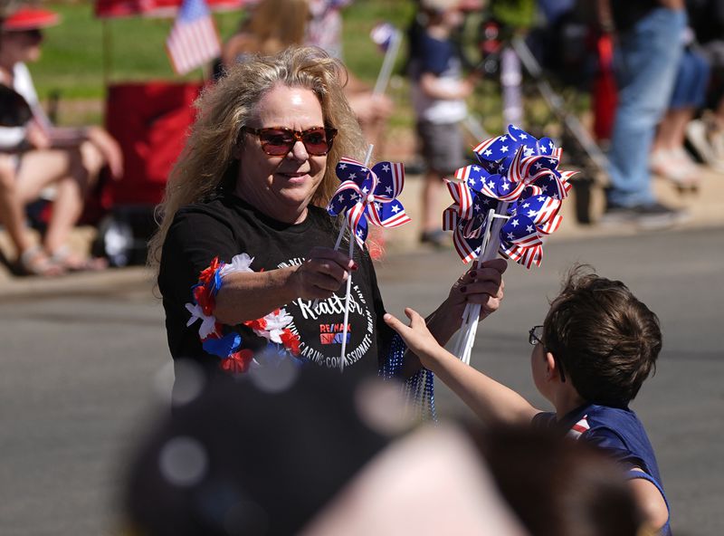 A woman hands out patriotic pinwheels during the Colorado 4th at Firestone parade to mark the Independence Day holiday Thursday, July 4, 2024, in Firestone, Colo. Floats, marching bands, classic cars and motorcycles were features in the annual parade through the Weld County community north of Denver. (AP Photo/David Zalubowski)