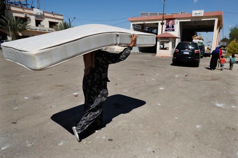 A Syrian woman fleeing the war in Lebanon carries a mattress as she arrives at the Syrian-Lebanese border crossing in Jousieh, Syria, Tuesday, Oct. 2, 2024. (AP Photo/Omar Sanadiki)