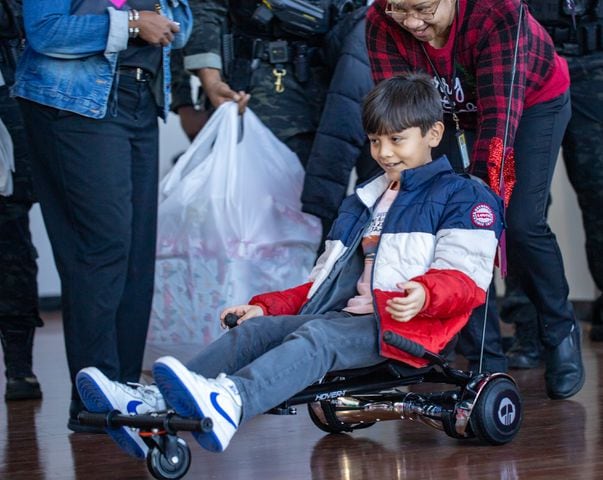 DeKalb County Sheriff’s Office holds the 16th annual Adopt-A-Family celebration on Tuesday, Dec 16, 2023 where Angel Suarez-Valencia 9, reacts to his new wheels during the party. Law enforcement officers donate their own money and buy gifts for about a dozen local children.  (Jenni Girtman for The Atlanta Journal-Constitution)