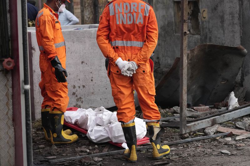 National Disaster Response Force rescuers stand near the dead body of a person after an explosion and fire at a chemical factory in Dombivali near Mumbai, India, Friday, May 24, 2024. Multiple people were killed and dozens were injured in the incident that happened Thursday. (AP Photo/Rajanish Kakade)