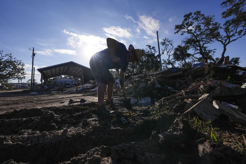 Chris Jordan, maintenance manager for Horseshoe Beach, tries to find a water shutoff valve amid the rubble of the destroyed city hall in the aftermath of Hurricane Helene, in Horseshoe Beach, Fla., Sunday, Sept. 29, 2024. (AP Photo/Gerald Herbert)