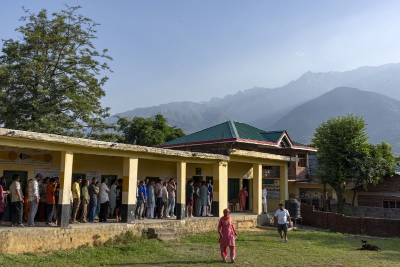 The sun rises behind the Dhauladhar range of the Himalaya as people form queues to cast their vote in the seventh and last round of polling in India's national election in Dharamshala, Saturday, June 1, 2024. (AP Photo/Ashwini Bhatia)