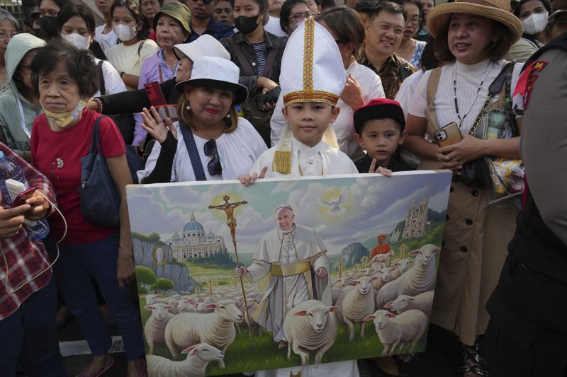 Worshipers hold a painting as they wait for Pope Francis outside the Cathedral of Our Lady of the Assumption, in Jakarta, Indonesia, Wednesday, Sept. 4, 2024.(AP Photo/Achmad Ibrahim )