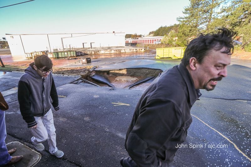 Carson Akney (left) and his father, Harry Akney, examine a sinkhole behind Atlanta Wholesale Company on Buford Highway. JOHN SPINK / JSPINK@AJC.COM