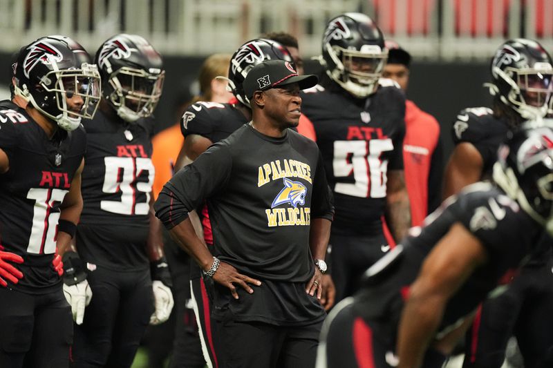 Atlanta Falcons head coach Raheem Morris, center, stands with his team while wearing an Apalachee High School T-shirt after a recent school shooting there before an NFL football game against the Pittsburgh Steelers on Sunday, Sept. 8, 2024, in Atlanta. (AP Photo/John Bazemore)