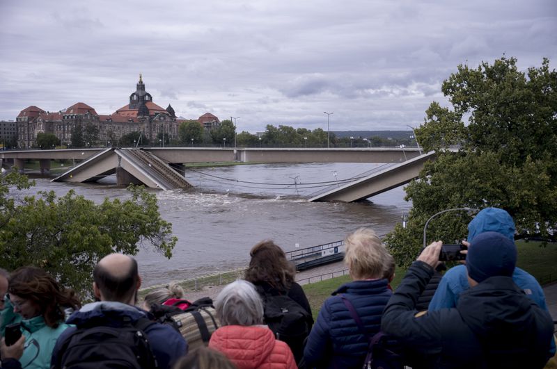 Spectators look at the partially collapsed Carolabrücke bridge over the Elbe, which is rising rapidly due to upcoming flood waters, in front of the state chancellery in Dresden, Germany, Sunday, September 15, 2024. (AP Photo/Markus Schreiber)