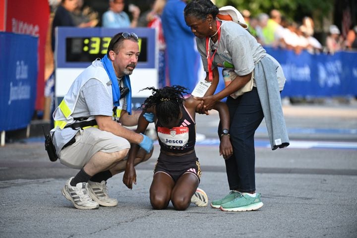 Jesca Chelanget is helped up after crossing the finish line during the 55th running of the Atlanta Journal-Constitution Peachtree Road Race on Thursday, July 4, 2024.  ( Hyosub.Shin / ajc.com)