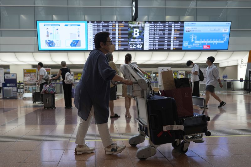 Passengers look at flight information as some flights were canceled due to a severe weather system affecting Japan, at Haneda airport Friday, Aug. 30, 2024, in Tokyo. (AP Photo/Eugene Hoshiko)