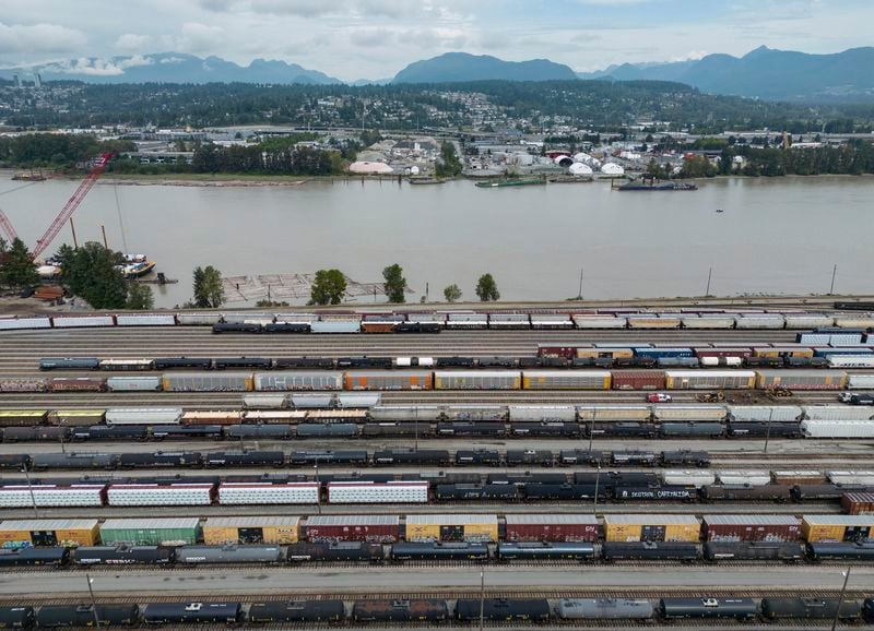 Train cars are seen on the tracks in an aerial view at Canadian National Rail's Thornton Yard as the Port Mann Bridge spans the Fraser River and trucks transport cargo containers on the highway in Surrey, British Columbia, Canada, Thursday, Aug. 22, 2024. (Darryl Dyck/The Canadian Press via AP)