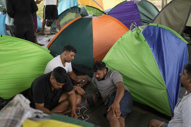 Migrants from Nepal use their phones at a camp for people who walked across the Darien Gap in hope of reaching the U.S., in Lajas Blancas, Panama, Thursday, Sept. 26, 2024. (AP Photo/Matias Delacroix)