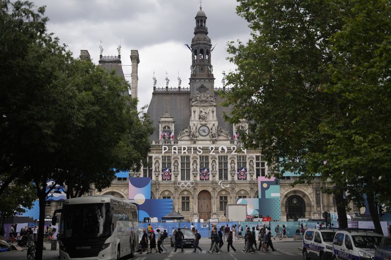 The logo of the Paris 2024 Olympic Games hangs from the facade of the Paris city hall, behind constructions barriers, Wednesday, July 3, 2024 in Paris. Just three weeks before the Olympics, the excitement that was building up in the host city has mingled with anxiety about France’s political future. (AP Photo/Thibault Camus)