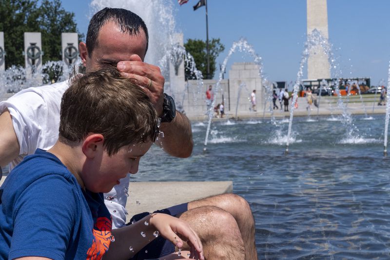 Rafael Fontana, 8, gets cooled off by his father Carlos Fontana, both from Chicago, at the Rainbow Pool at the World War II Memorial, Friday, June 21, 2024, in Washington. Temperatures are forecast to reach 100 degrees on Saturday. (AP Photo/Alex Brandon)