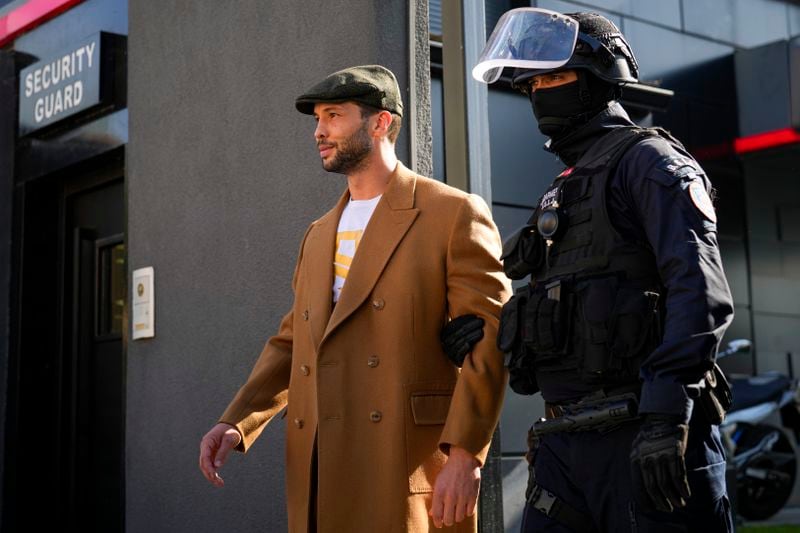 Tristan Tate exits his residence convoyed by a masked gendarme for questioning after a police search raid, on the outskirts of Bucharest, Romania, Wednesday, Aug. 21 2024. Masked police officers in Romania carried out fresh raids early Wednesday at the home of divisive internet influencer Andrew Tate, who is awaiting trial on charges of human trafficking, rape and forming a criminal gang to sexually exploit women.(AP Photo/ Vadim Ghirda)