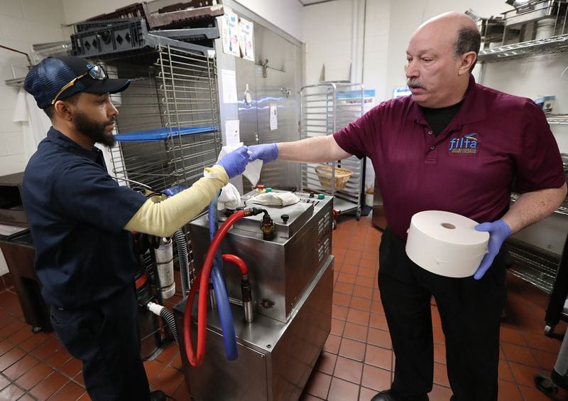Filta franchise owner John Lopez hands lead technician Donnell Collier a new sock and filter for their mobile filtration unit to filter fry oil while working at a concession stand in the Georgia World Congress Center on Thursday, Jan. 17, 2019, in Atlanta.