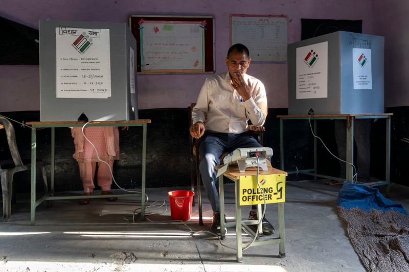 A polling official looks at his device for confirmation as a voter casts her vote in a bye-election after voting in the seventh and last round of polling in India's national election in Dharamshala, India, Saturday, June 1, 2024. (AP Photo/Ashwini Bhatia)
