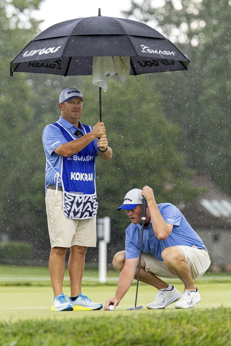 Caddie Malcolm Baker, left, holds an umbrella as Talor Gooch, right, of Smash GC, lines up a putt on the seventh green during the final round of LIV Golf Greenbrier at The Old White at The Greenbrier, Sunday, Aug. 18, 2024, in White Sulphur Springs, W.Va.. (Scott Taetsch/LIV Golf via AP)