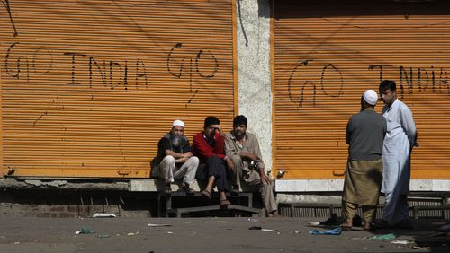 Kashmiris sit outside closed shops painted with graffiti during a curfew in central Srinagar, India, Thursday, Sept. 16, 2010. (AP Photo/Dar Yasin, File)