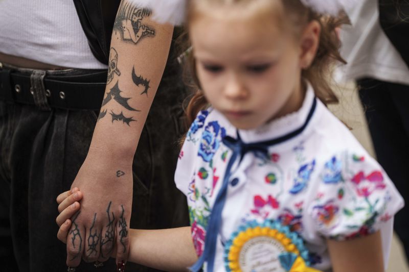 A first-grade girl holds the hand of her older schoolmate and walks to the traditional ceremony for the first day of school in Zaporizhzhia, Ukraine, Sunday Sept. 1, 2024. Zaporizhzhia schoolchildren celebrated the traditional first day of school near the frontline. With the front just 40 kilometers away, the war is never far from the minds of teachers and families. (AP Photo/Evgeniy Maloletka)