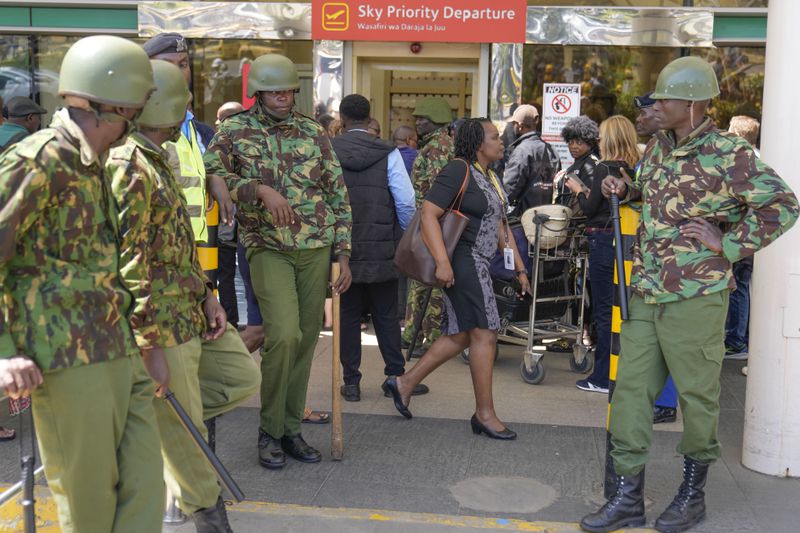 Kenya anti riot police stand guard as stranded passengers wait for their delayed flights out of JKIA airport after flights were grounded following workers’ protesting a planned deal between the government and a foreign investor, in Nairobi, Kenya, Wednesday, Sept. 11, 2024. (AP Photo/Brian Inganga)