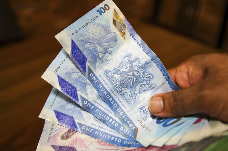 A vendor holds a handful of Trinidad and Tobago dollars, in Port-of-Spain, Trinidad and Tobago, Tuesday, Aug. 20, 2024. Prime Minister Keith Rowley announced Sunday, Aug. 18, 2024, the country is redrawing the island's coat of arms to remove references to European colonization and that Christopher Columbus' three ships will be replaced with the steelpan, a popular percussion instrument. (AP Photo/Ash Allen)