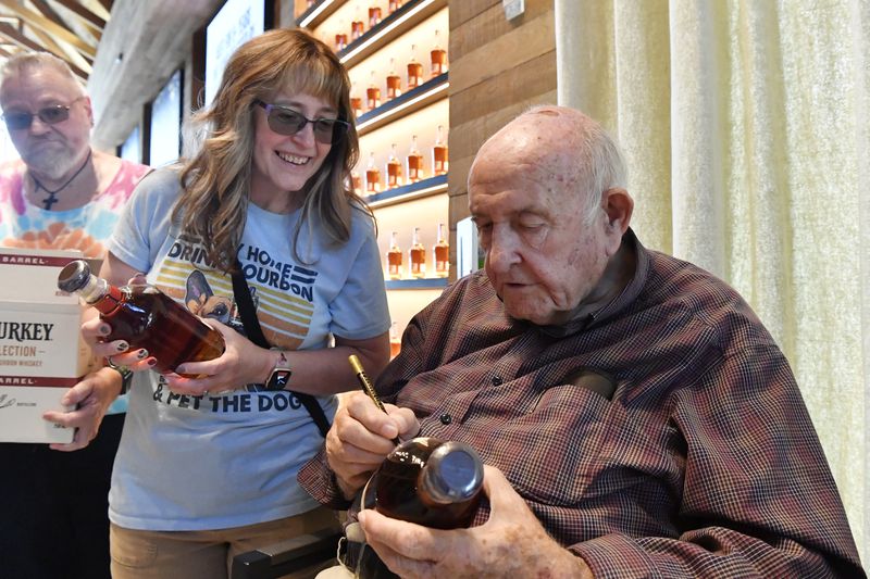 Donna Barton, left, of Princeton, W. Va., has 89-year-old Jimmy Russell, known as the "Buddha of Bourbon" sign a bottle of bourbon in the Visitors' Center at the Wild Turkey Distillery in Lawrenceburg, Ky., Wednesday, Aug. 28, 2024. (AP Photo/Timothy D. Easley)