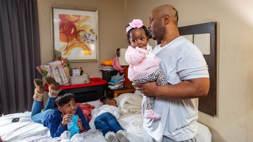 The White girls, including Mckenzie, 10, from left, Legend, 4 (sleeping) and 5-month-old Justice greet their father Melvin, right, after he comes home to their extended-stay hotel room Wednesday, Dec 21, 2022.  The family has lived in extended-stay hotels for years.  Despite Melvin working full-time, they canÕt find long-term safe housing they can afford.  (Jenni Girtman for The Atlanta Journal-Constitution)