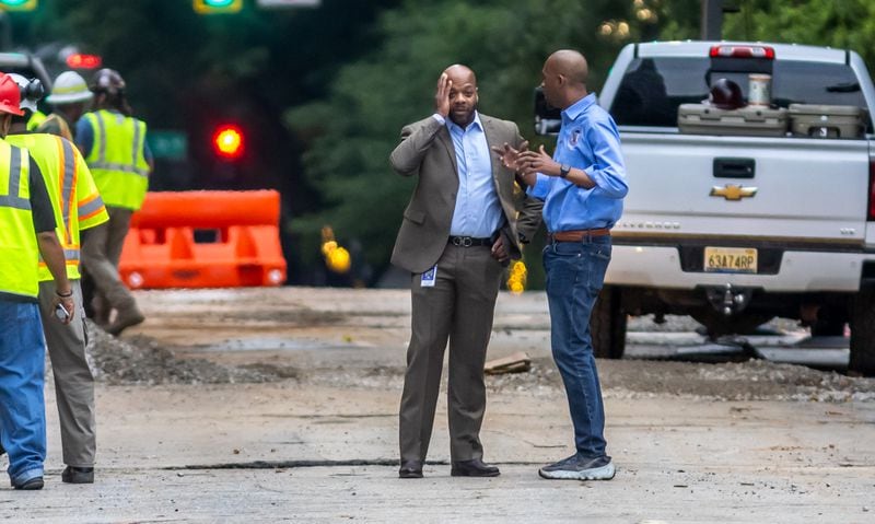 Watershed Commissioner Al Wiggins, Jr. (left) and City Council Member Antonio Lewis (right) confer on West Peachtree Street as workers continue to put finishing touches on the water-filled main hole on Wednesday morning, June 5, 2024 after the city announced that water had been restored after the break at West Peachtree Street and 11th Street.  The city said the system was slowly being brought back online to “allow pressures on the system to build.”  (John Spink/AJC)