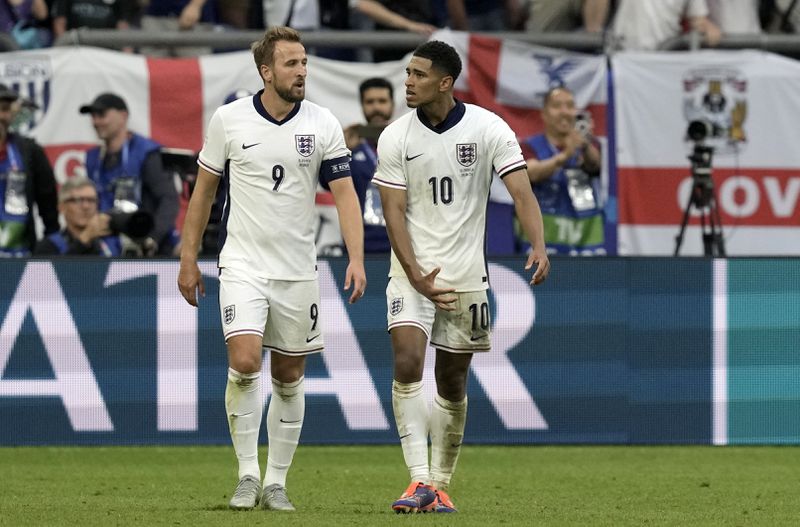 EDS NOTE: OBSCENITY - England's Jude Bellingham, right, gestures as he stands next to Harry Kane after scoring his side's first goal during a round of sixteen match between England and Slovakia at the Euro 2024 soccer tournament in Gelsenkirchen, Germany, Sunday, June 30, 2024. Bellingham is being investigated by UEFA over a potentially offensive gesture made during a European Championship win against Slovakia. . (AP Photo/Thanassis Stavrakis)