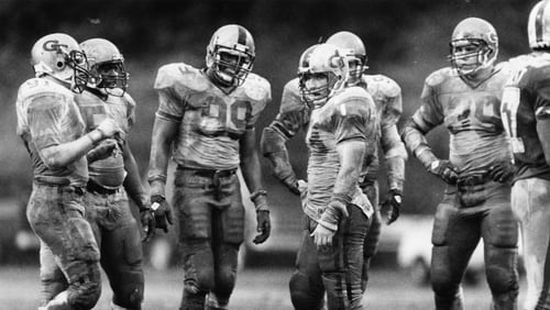 Ted Roof (center), Pat Swilling (99) and other Georgia Tech defensive players are soaked in mud during a game against Duke in 1985. Incoming Georgia Tech freshman Bruce Jordan-Swilling and Tre Swilling give Roof, now Tech’s defensive coordinator, a large amount of credit for their choosing to become Yellow Jackets. (Andy Sharp / AJC file)