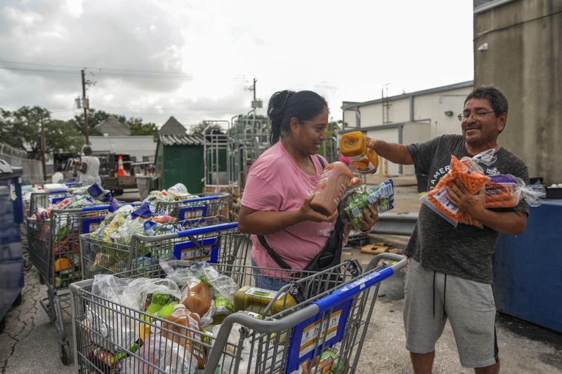 East End residents Laura and Jose Galvan sift through perishable foods that were left outside of a Kroger due to power outages from the recent Hurricane Beryl that made landfall in Houston on Tuesday, July 9, 2024. (Raquel Natalicchio/Houston Chronicle via AP)