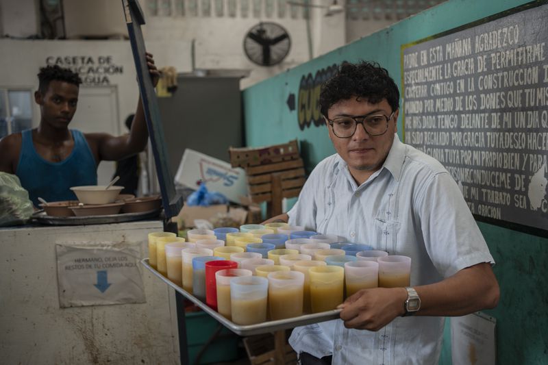 Josue Martinez serves juice to migrants during lunch at the Peace Oasis of the Holy Spirit Amparito shelter in Villahermosa, Mexico, Friday, June 7, 2024. "Mexico is the wall," said Martínez, a psychologist at the only shelter in Villahermosa. "(The migrants) are trapped in the south," referring to Mexican authorities' tactic of wearing migrants out until they can no longer continue. (AP Photo/Felix Marquez)