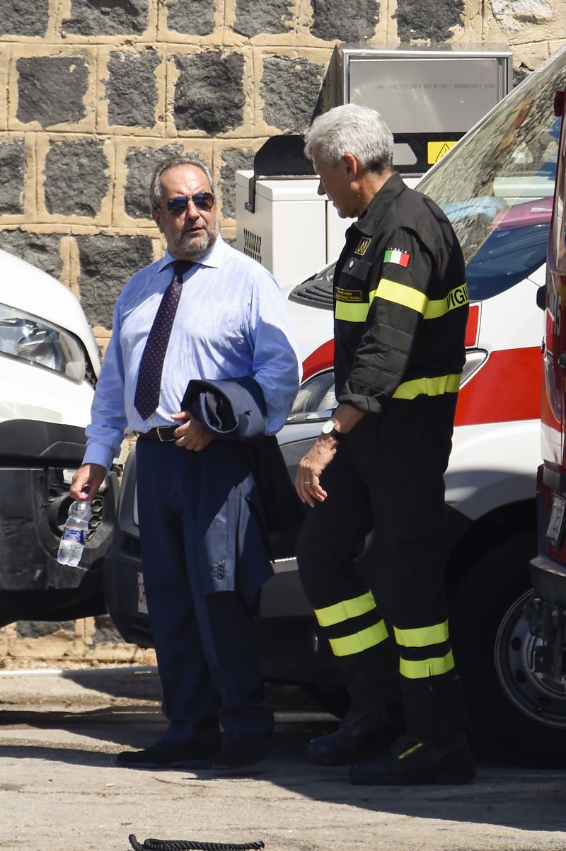 Prefect of Palermo, Massimo Mariani, left, is flanked by a firefighter as he arrives at the harbor in Porticello, Sicily, southern Italy, Thursday, Aug. 22, 2024. Divers searching the wreck of the superyacht Bayesian that sank off Sicily on Monday recovered a fifth body on Thursday and continued to search for one more as investigators sought to learn why the vessel sank so quickly. (AP Photo/Salvatore Cavalli)