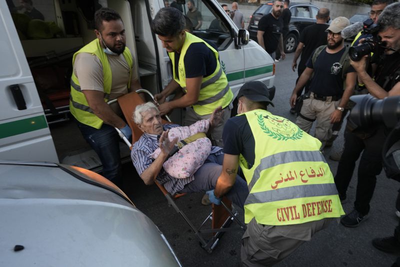 Civil defense workers carry an elderly, fleeing the south, as he arrives at a school turned into a shelter in Beirut, Monday, Sept. 23, 2024. (AP Photo/Bilal Hussein)