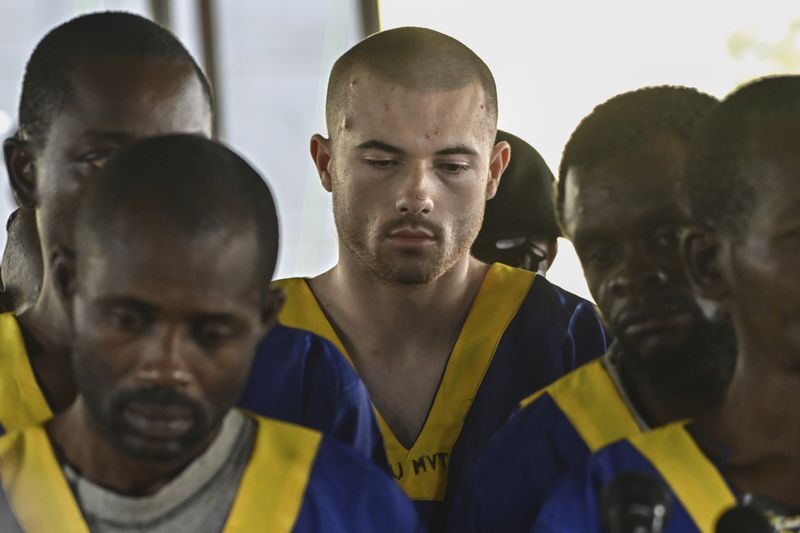 American Tyler Thompson Jr, center, sits in court in Kinshasa, Friday, June 7, 2024. Three Americans accused of a role in last month's attempted coup in Congo appeared in court in Kinshasa on Friday, among a total of 53 defendants who were lined up on plastic chairs before the judge on the first day of the hearing. (AP Photo/Samy Ntumba Shambuyi)